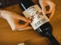 Mani che applicano un'etichetta su una bottiglia di vino. L'etichetta indica "Toscana", la regione di origine del vino Sangiovese.