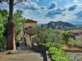 Una persona scende una scalinata in pietra, con case antiche e vegetazione rigogliosa. In lontananza, il **monte Morello** domina il paesaggio collinare.