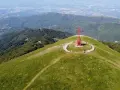 La croce del Pratomagno domina un paesaggio verdeggiante, con montagne boscose e una città in lontananza.