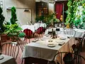Cortile di un ristorante, tavoli apparecchiati con tovaglie bianche e rosse, piante verdi e sedie nere. Un invito a mangia e bevi santo spirito.