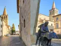 Statua di donne al lavoro, con campanili e palazzi storici sullo sfondo. Un assaggio di cosa vedere a Sansepolcro.