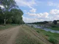 Sentiero lungo il fiume con alberi e il masso della Gonfolina in lontananza. Cielo azzurro con nuvole bianche.