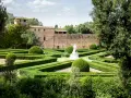 Giardini geometrici a San Quirico d'Orcia con statua bianca e edifici storici sullo sfondo.