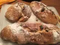 Tre panini aretini dorati, cosparsi di zucchero a velo e uvetta, pronti per essere gustati.