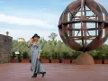 Donna con cappello nero ammira l'Uomo Vitruviano in una sfera di legno, un'opera iconica da vedere a Vinci, con colline verdi sullo sfondo.