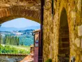 Arco in pietra che incornicia un panorama collinare toscano, con cipressi e vigneti, tipico dei borghi del Chianti.