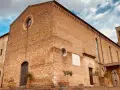 La **chiesa di Sant'Agostino** a San Gimignano, con la sua facciata in mattoni rossi e il campanile svettante, si staglia contro un cielo azzurro e nuvoloso.