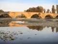 Ponte romanico con archi a tutto sesto, riflesso sull'acqua calma. I Setteponti di Arezzo, un'antica via, abbraccia la campagna toscana.