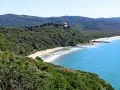 Vista panoramica delle bandite di Scarlino, con una spiaggia dorata bagnata da un mare azzurro e una villa in cima a una collina verde.