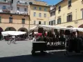 Mercato all'aperto nella piazza delle vettovaglie, con bancarelle di abbigliamento e persone che passeggiano.