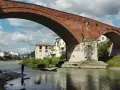 Ponte Mediceo a Pontassieve, cosa vedere: un pescatore sul fiume Sieve sotto l'arco in mattoni rossi, con case colorate sullo sfondo.