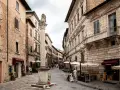 A stone column with a lion statue stands in a cobblestone street lined with historic buildings and shops.