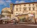 Mercatino dell'antiquariato in piazza grande, con opere d'arte, sculture e mobili antichi esposti sotto il sole.