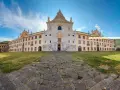 La maestosa Certosa di Calci si erge sotto un cielo azzurro, con un sentiero di pietra che conduce alla sua imponente facciata.