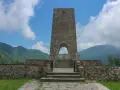Monumento a Sant'Anna di Stazzema, cosa vedere: un imponente torrione in pietra con arco, che custodisce una tomba, circondato da mura e montagne.