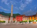 Piazza con obelisco e leoni, edifici colorati e montagne sullo sfondo. Un'idea di cosa vedere a Marina di Massa.