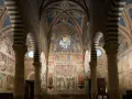 Interno del duomo di San Gimignano, con affreschi medievali che narrano storie sacre, volte a crociera a strisce bianche e nere e un rosone colorato.