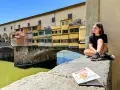 Ragazza con capelli rosa seduta sul Ponte Vecchio a Firenze, con una guida per bambini in primo piano.