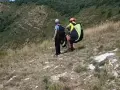 Due parapendisti si preparano al decollo sulla **Valle del Serchio**, con un paesaggio verdeggiante alle spalle.