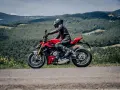 Motociclista in tuta rossa e nera sfreccia su una Ducati rossa lungo il passo del giogo, tra colline verdi e cielo azzurro.