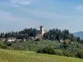 Un borgo collinare con un castello domina il paesaggio toscano di Scarperia e San Piero, circondato da cipressi e ulivi.