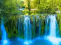 Cascata rigogliosa nel Val d'Arno, con acqua azzurra che scende su rocce ricoperte di muschio verde.