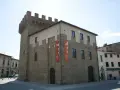 Il cassero di Montevarchi, un'antica torre con merlature, si erge imponente accanto a edifici storici, con bandiere rosse che adornano la facciata.