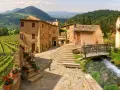 Monticchiello: cosa vedere? Un borgo toscano con vigneti, case in pietra, un ruscello e un ponte di legno.