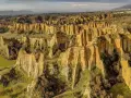Paesaggio surreale nella provincia di Arezzo, con calanchi dorati che si ergono tra colline verdi e alberi spogli.