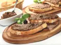 Toasted bread slices topped with dark spread, garnished with basil, olives, and capers.
