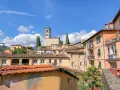 Panoramica di Barga, Lucca, con case colorate e il Duomo in cima alla collina sotto un cielo azzurro con nuvole bianche.