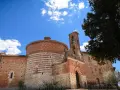 L'abbazia di San Galgano, con la sua rotonda in mattoni a fasce bianche e rosse, si staglia sotto un cielo azzurro con nuvole bianche.