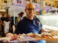 Uomo sorridente al mercato delle vettovaglie Livorno, offre un tagliere di salumi e formaggi.