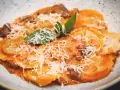 Tordelli versiliesi in un piatto bianco, conditi con sugo rosso, funghi, parmigiano grattugiato e basilico fresco.