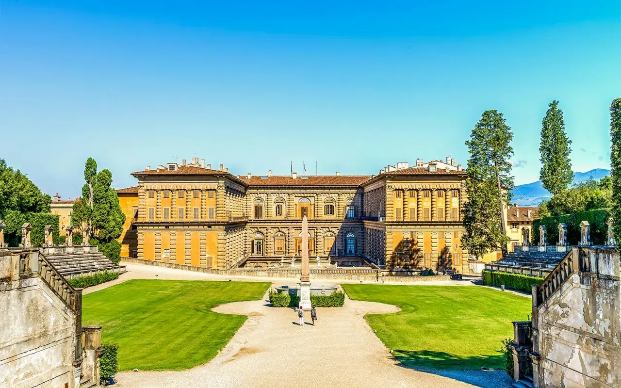 Il maestoso Palazzo Pitti si staglia contro un cielo azzurro, circondato da giardini curati e scalinate imponenti.