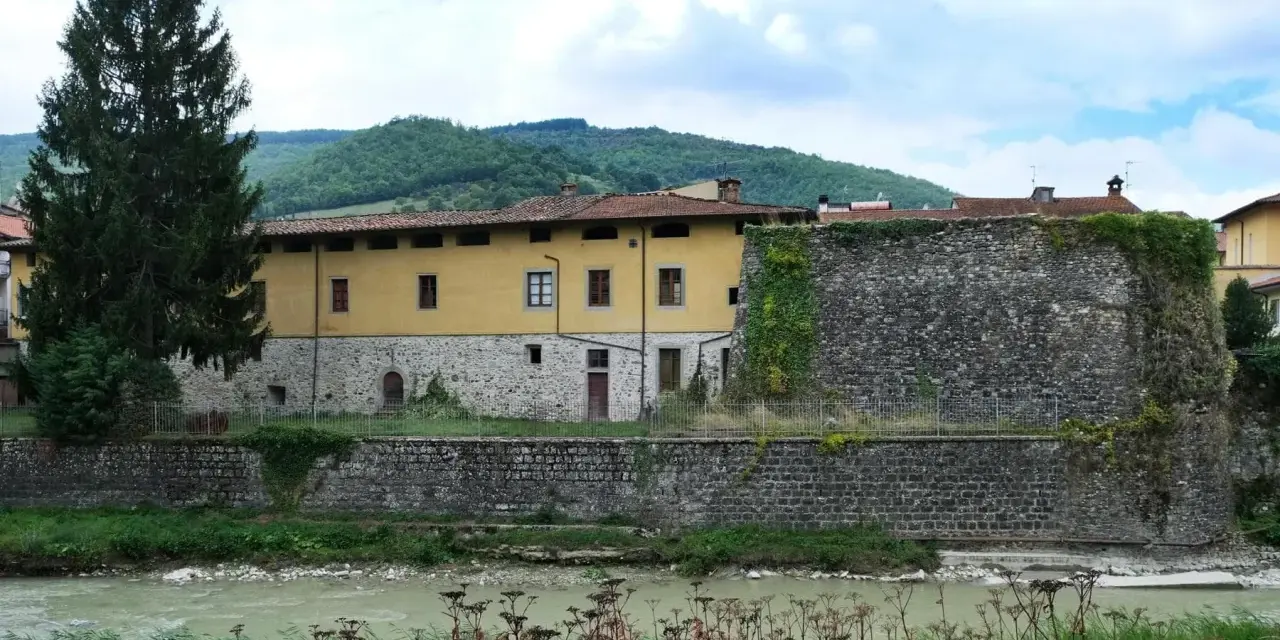 Pieve Santo Stefano: cosa vedere? Antica cinta muraria e palazzo storico affacciati sul fiume, tra colline verdi.