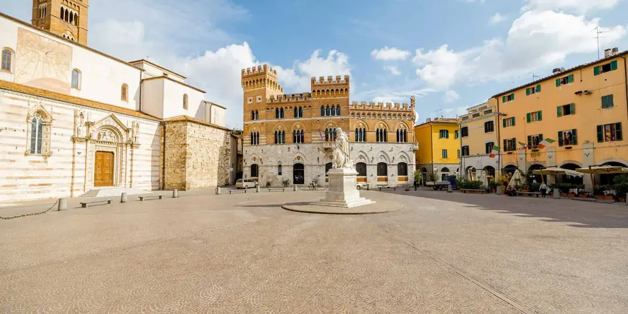 Piazza del Popolo a Grosseto, Italia, con il Duomo, il Palazzo Aldobrandeschi e case colorate.