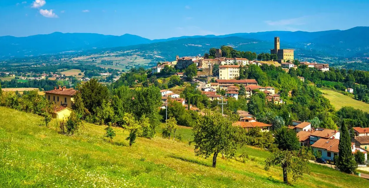 Borgo medievale in collina, un gioiello del Casentino cosa vedere. Case con tetti rossi, verde rigoglioso e un cielo azzurro intenso.