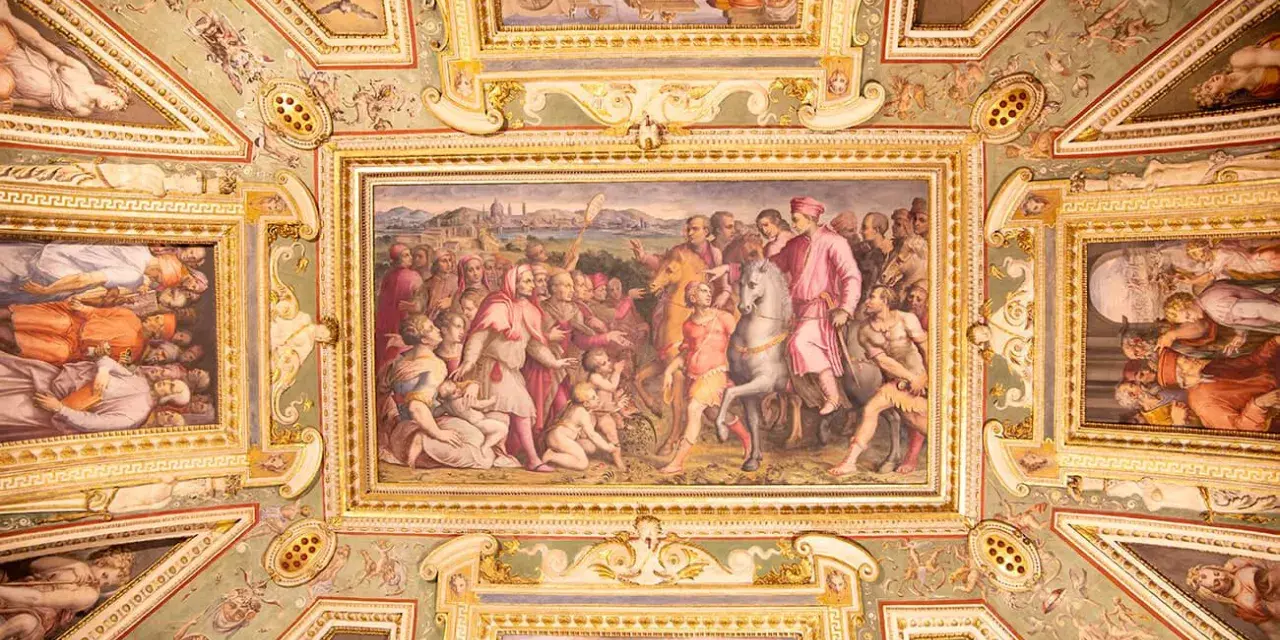 Soffitto affrescato con scene storiche e figure mitologiche, un capolavoro che evoca la grandezza del **Palazzo Vecchio**.