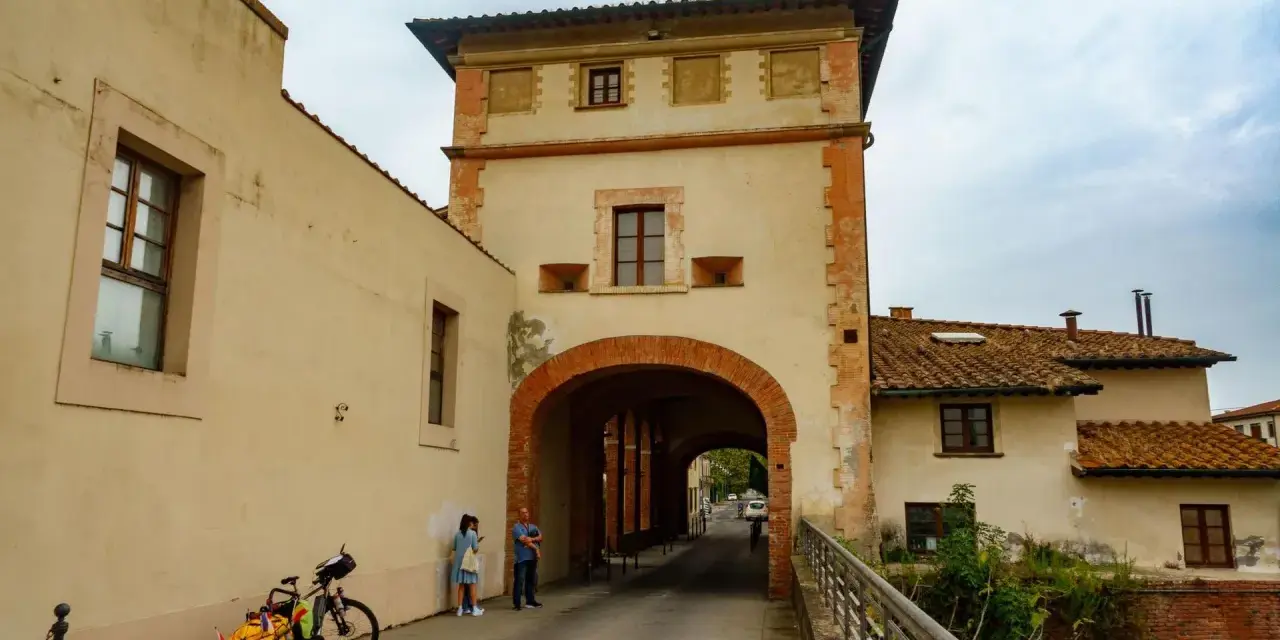 Un arco imponente a Santa Maria a Monte, con una coppia che osserva la strada. Una bici carica attende.