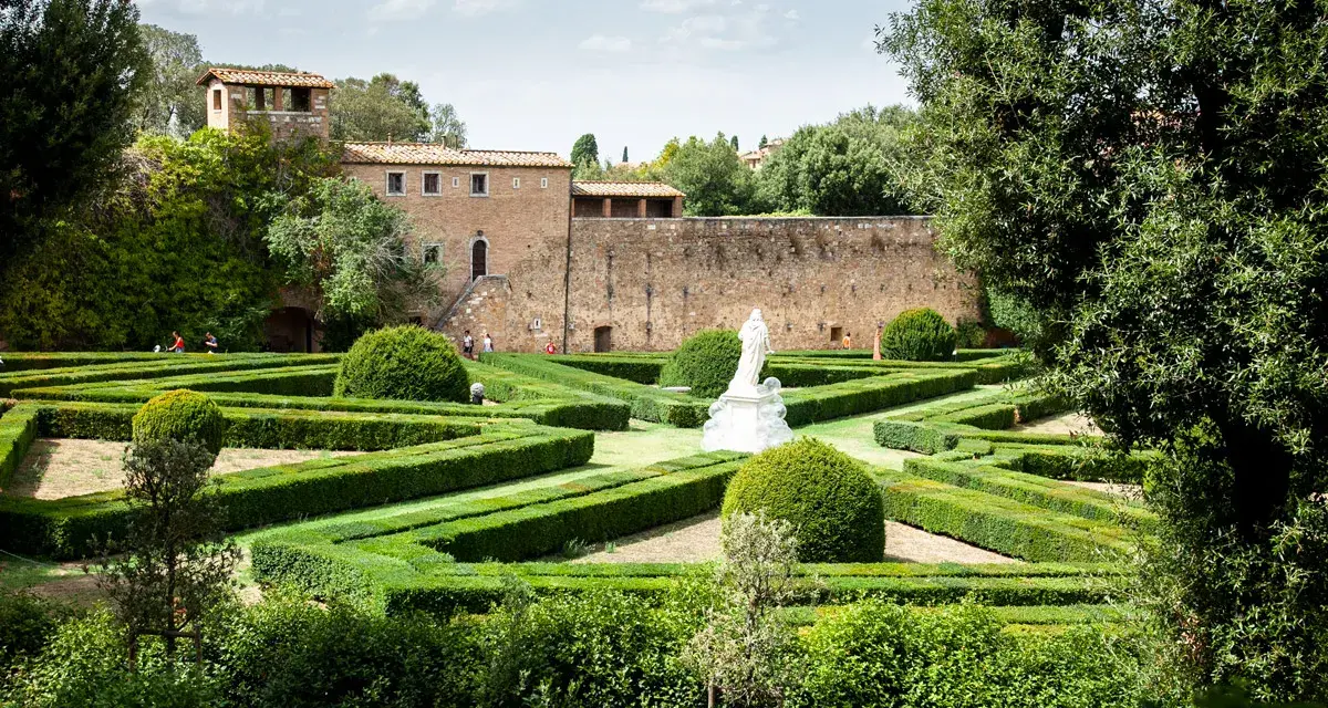 Giardini geometrici a San Quirico d'Orcia con statua bianca e edifici storici sullo sfondo.