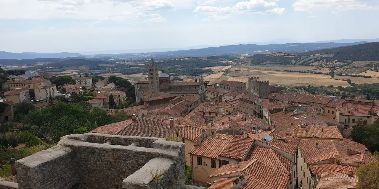 Panoramica di Massa Marittima con tetti rossi, una cattedrale imponente e colline toscane sullo sfondo.