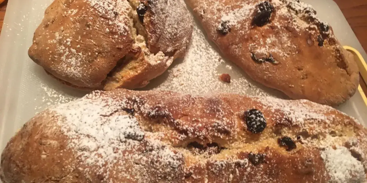 Tre panini aretini dorati, cosparsi di zucchero a velo e uvetta, pronti per essere gustati.