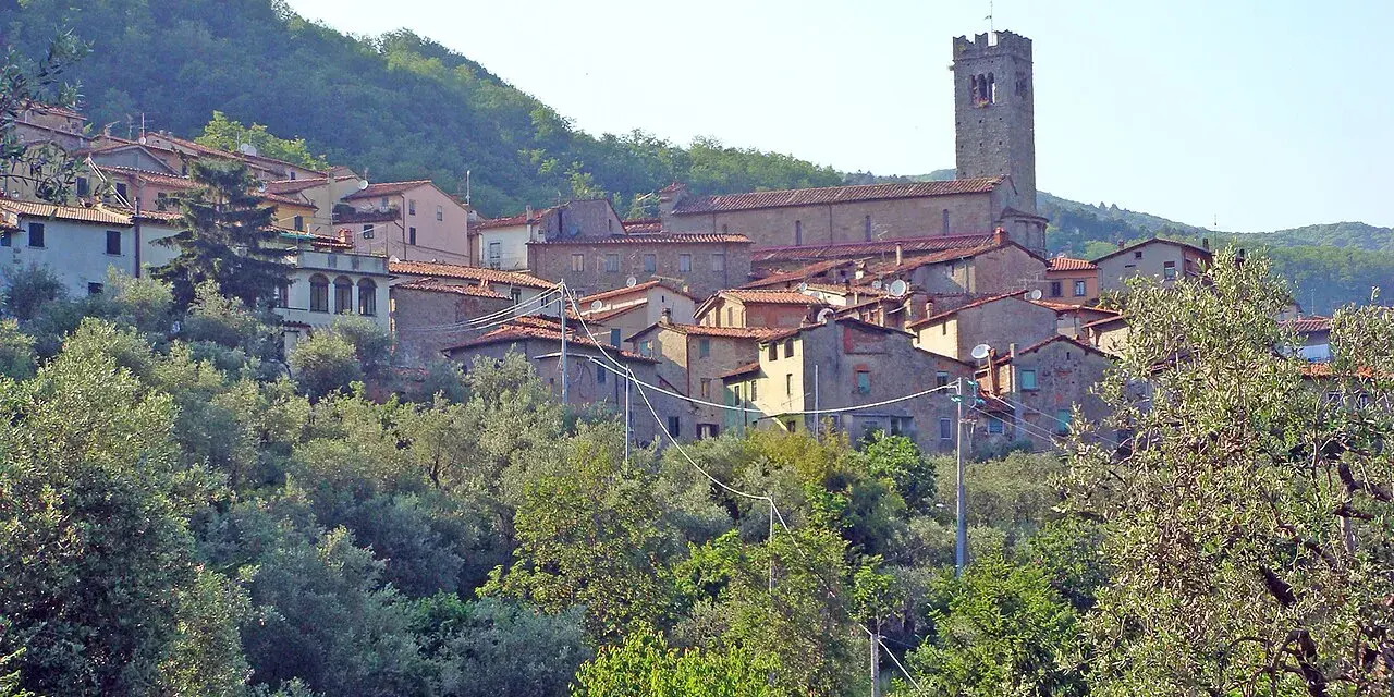 Antica villa basilica con torre campanaria, immersa nel verde di una collina toscana.