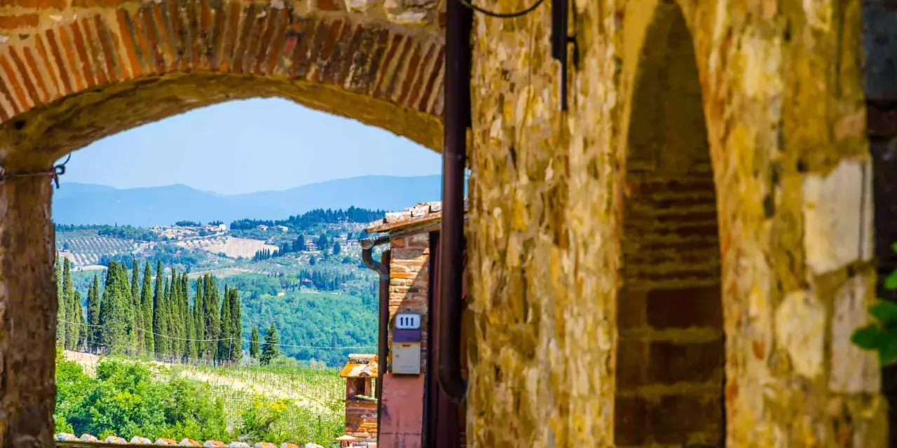 Arco in pietra che incornicia un panorama collinare toscano, con cipressi e vigneti, tipico dei borghi del Chianti.