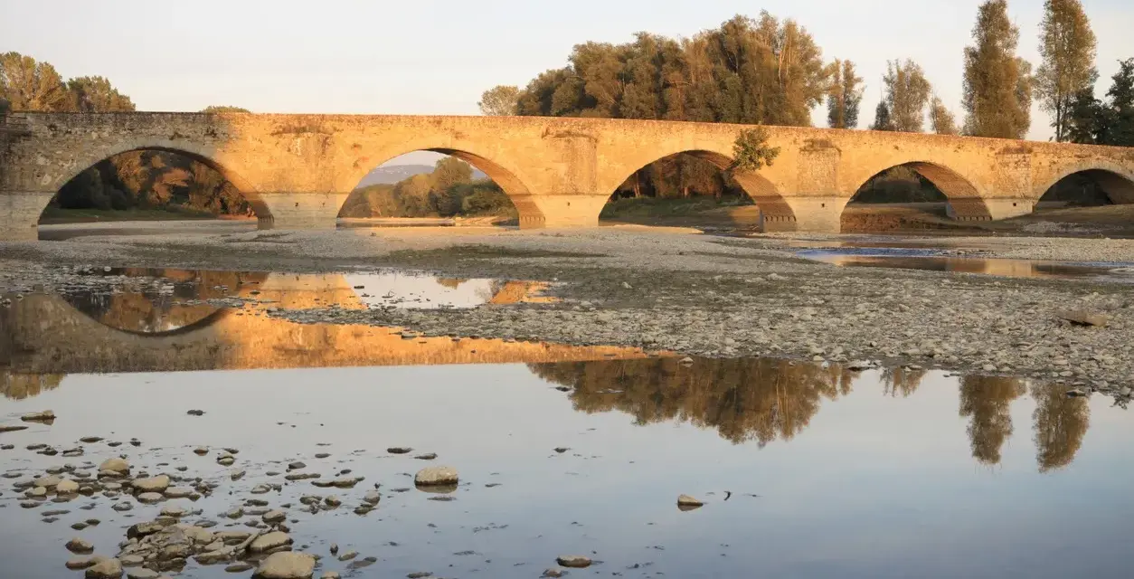 Ponte romanico con archi a tutto sesto, riflesso sull'acqua calma. I Setteponti di Arezzo, un'antica via, abbraccia la campagna toscana.