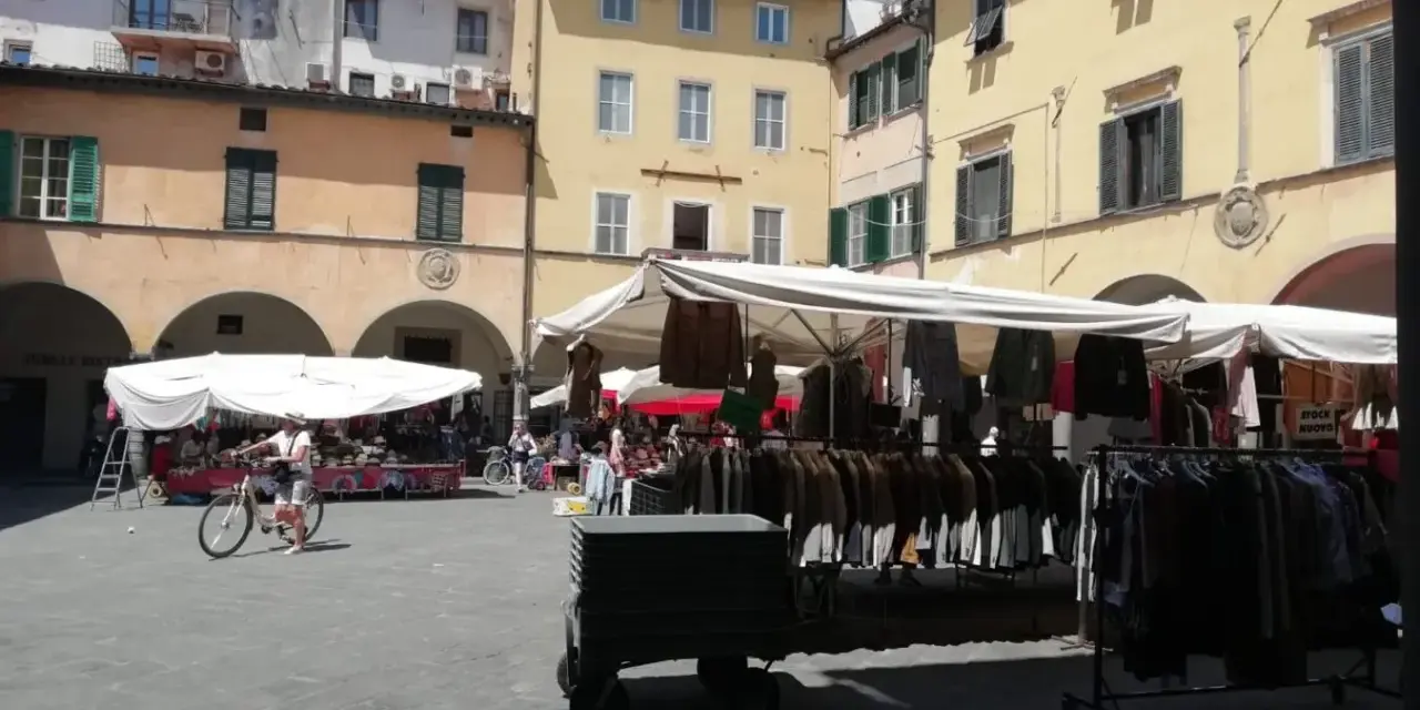 Mercato all'aperto nella piazza delle vettovaglie, con bancarelle di abbigliamento e persone che passeggiano.