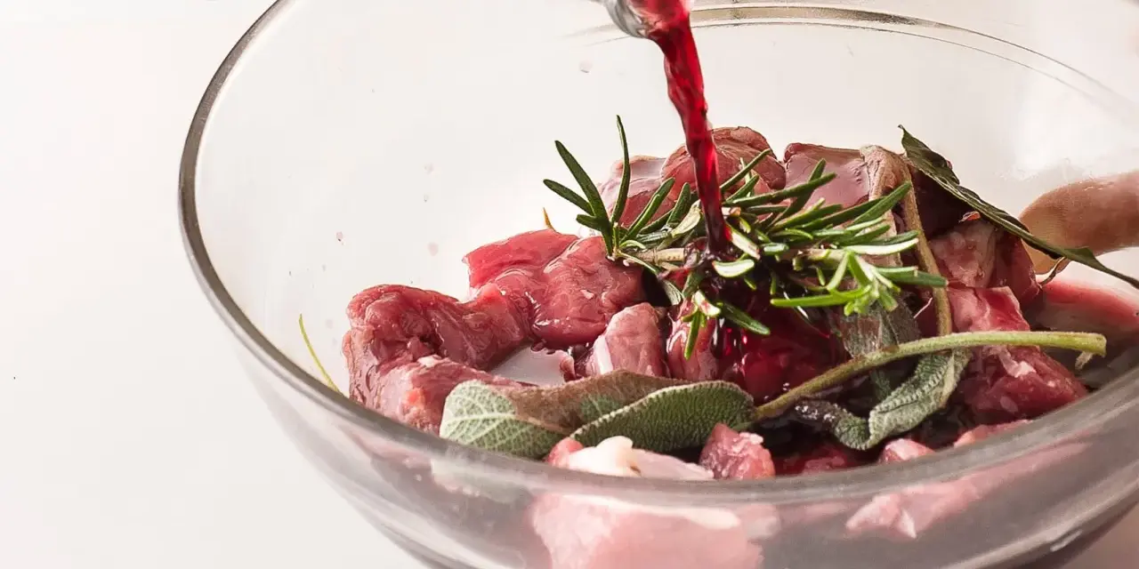 Vino rosso versato su cubetti di carne e aromi per macerare cinghiale.