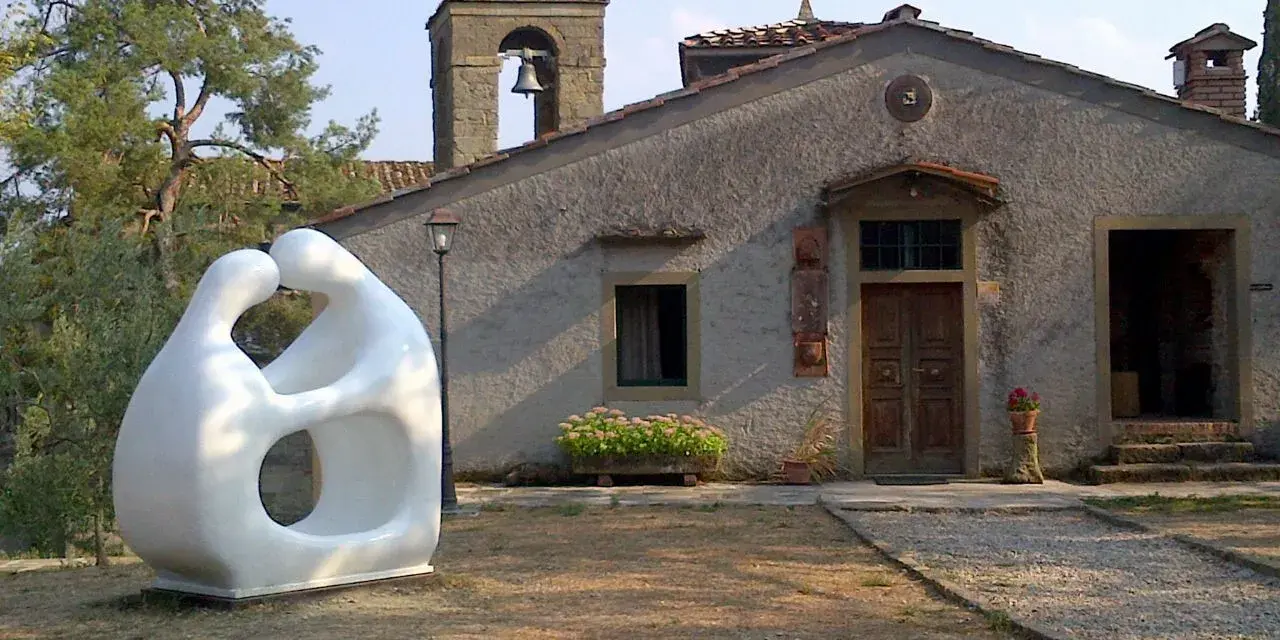 Scultura moderna di due figure abbracciate, simbolo di romena accoglienza, davanti a un edificio con campanile.