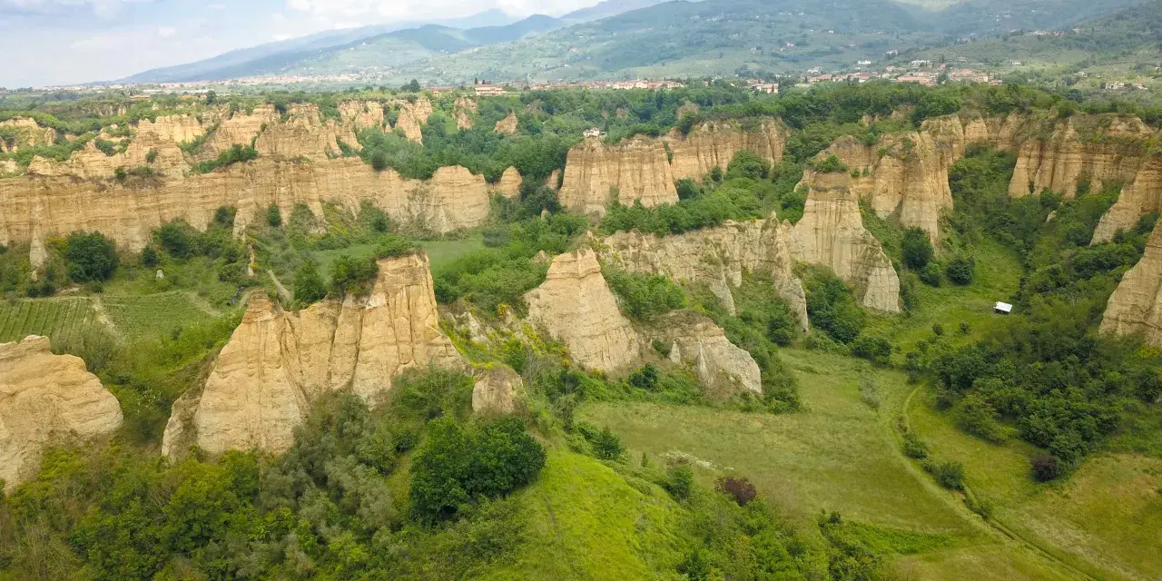 Le suggestive balze del Valdarno, scolpite dal tempo, si ergono tra verdi colline e un borgo in lontananza.